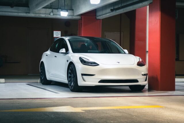 White Tesla parked in a dimly lit garage.