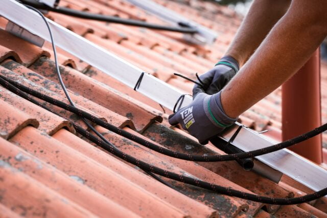 Roofer securing cables on a tiled roof.